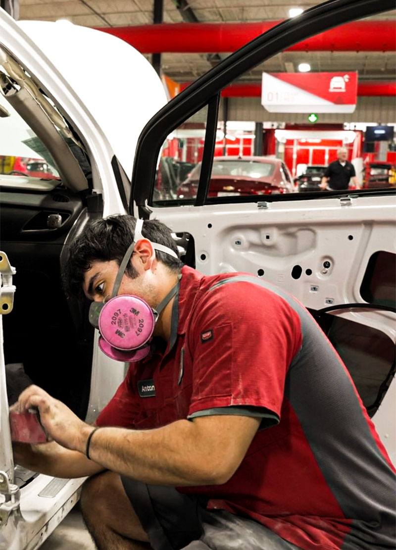 Auto repair technician wearing a pink respirator working on a vehicle's interior in a Swift Collision workshop, showcasing expert vehicle repair services.